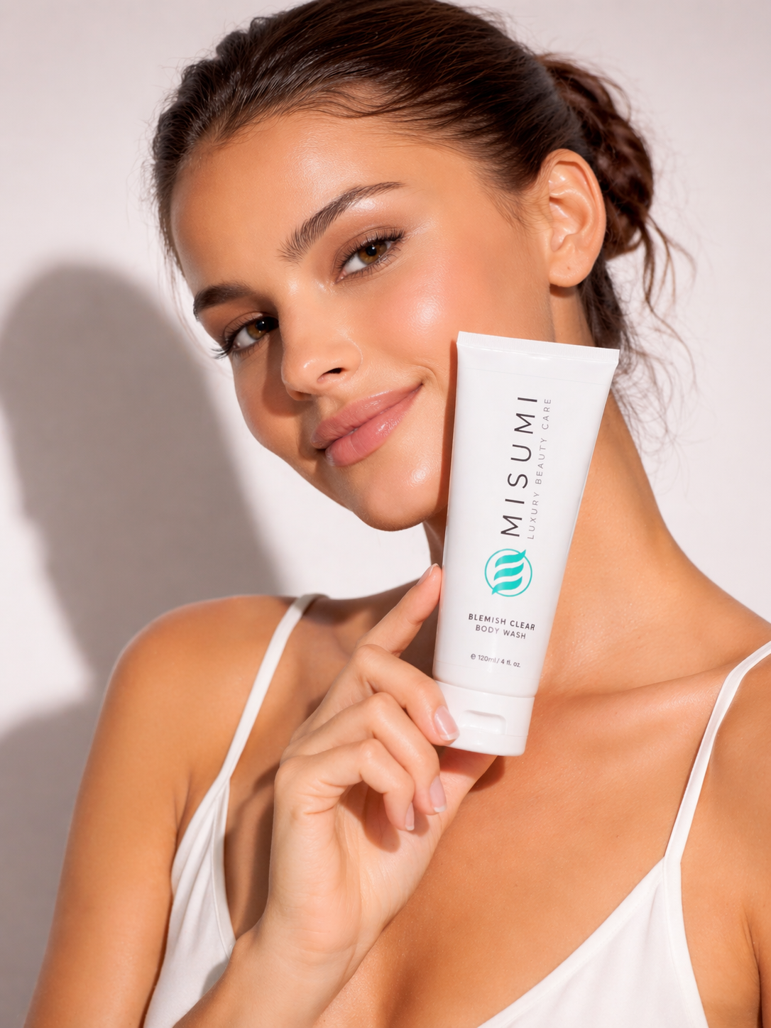 a model holding the MISUMI Blemish Clear Body Wash (120ml) tube with a glowing complexion, showing off healthy skin.
